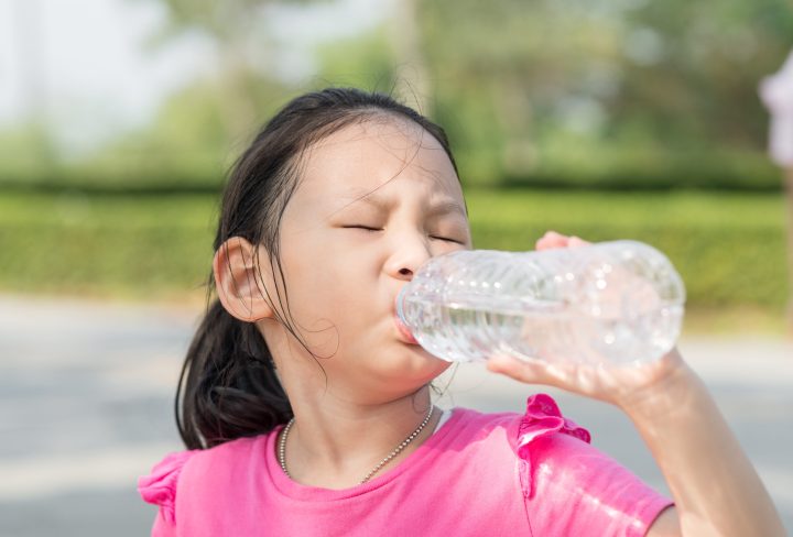 Happy Asian girl drinking a bottle of water outdoor.